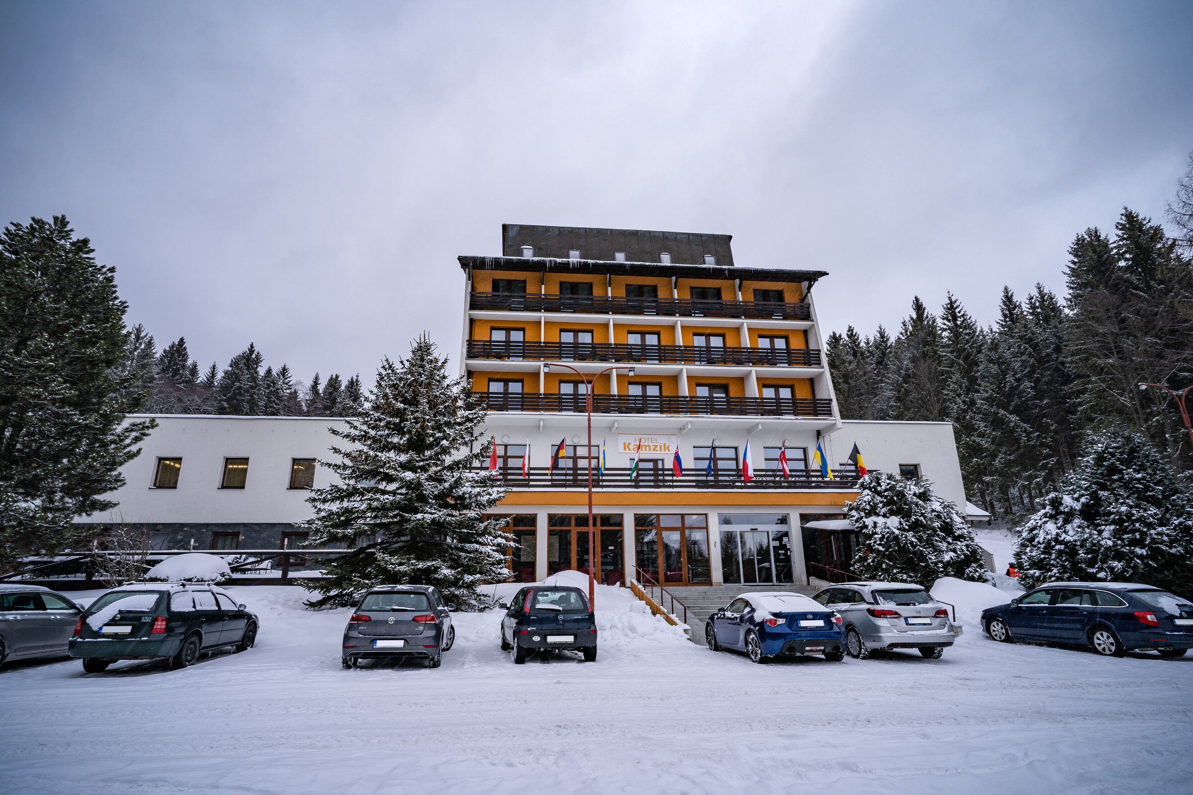 A multi-story hotel with a central entrance, surrounded by snow-covered trees and parked cars.