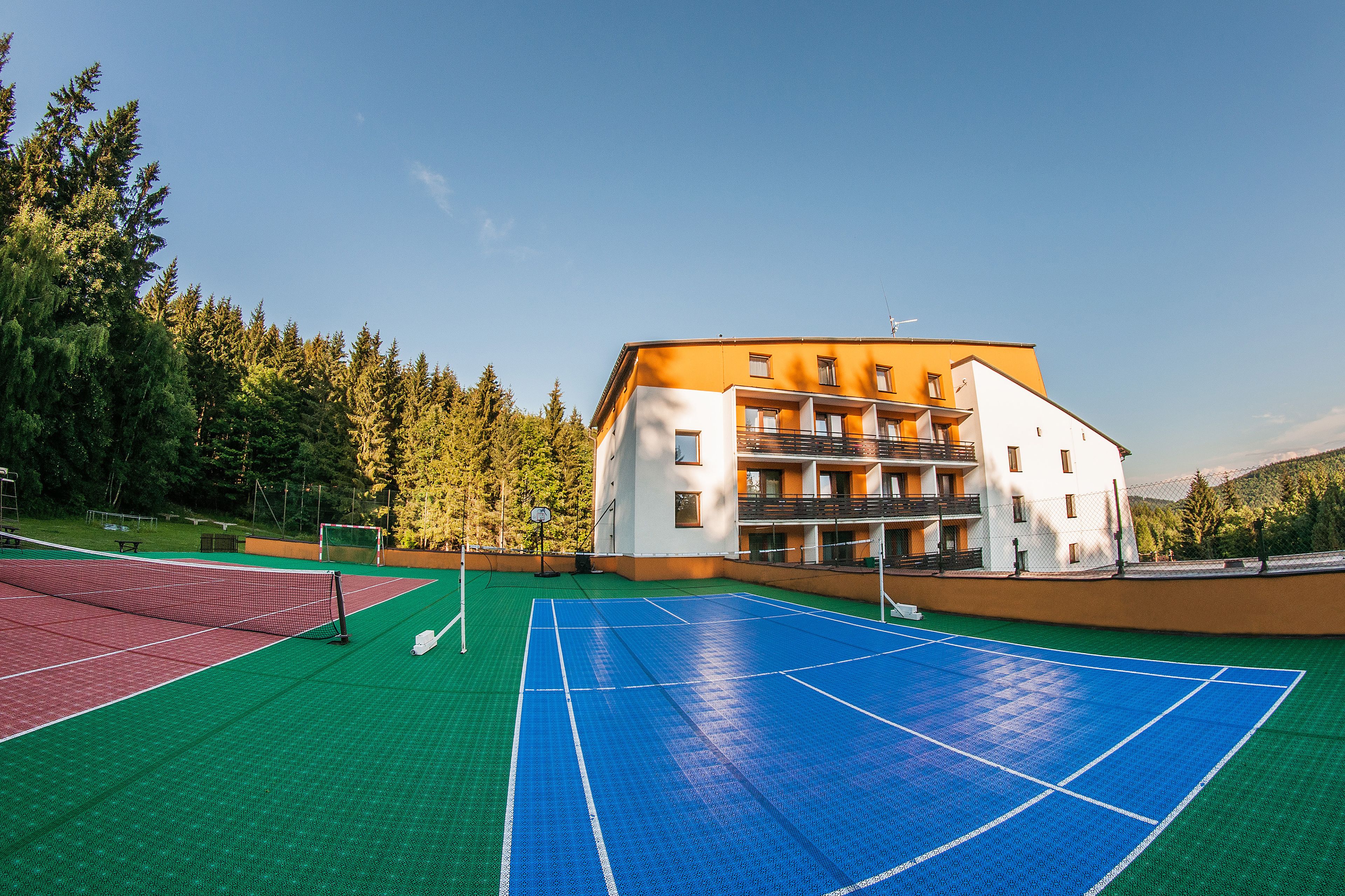 An outdoor tennis court adjacent to a multi-story building with balconies, surrounded by trees.