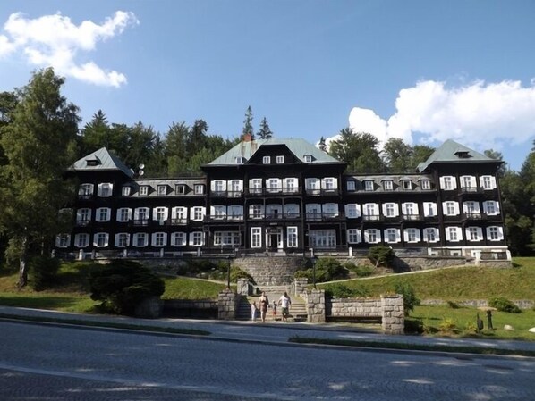 A large, multi-story building with a symmetrical facade, multiple windows, and a central entrance with steps. - Hotel Kamzík (Mala Moravka)