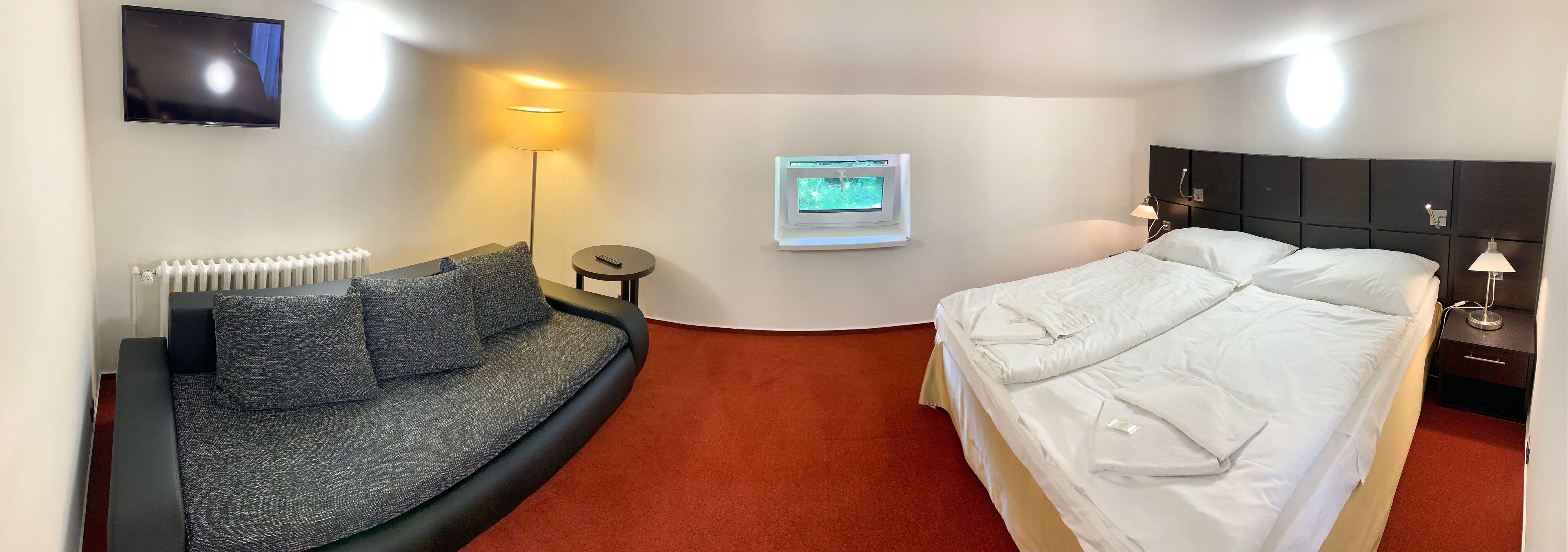 A hotel room with a sofa, a bed, a TV, a window, and a lamp.