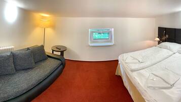 A hotel room with a sofa, a bed, a TV, a window, and a lamp.