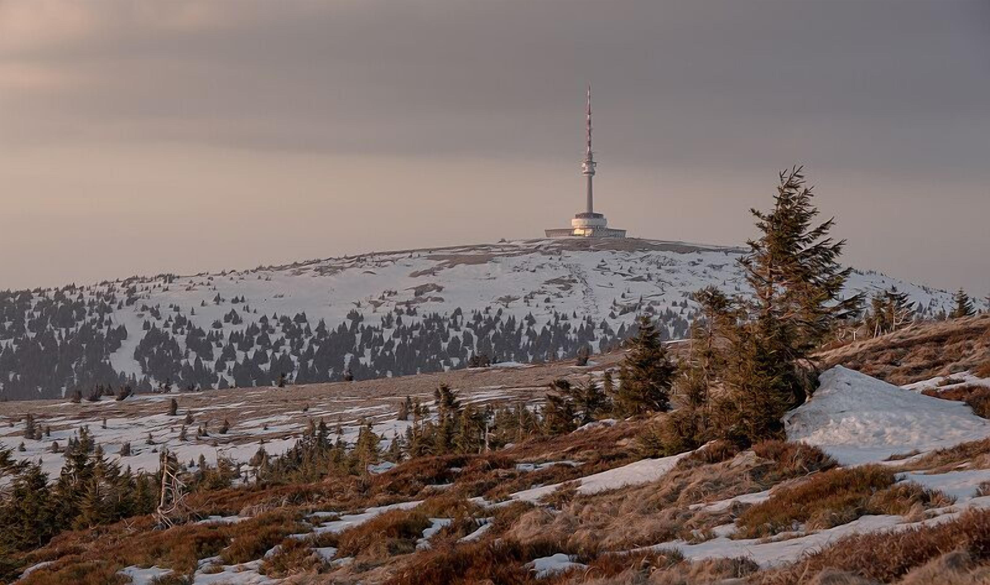 A snow-covered mountain with a tall tower and sparse trees.