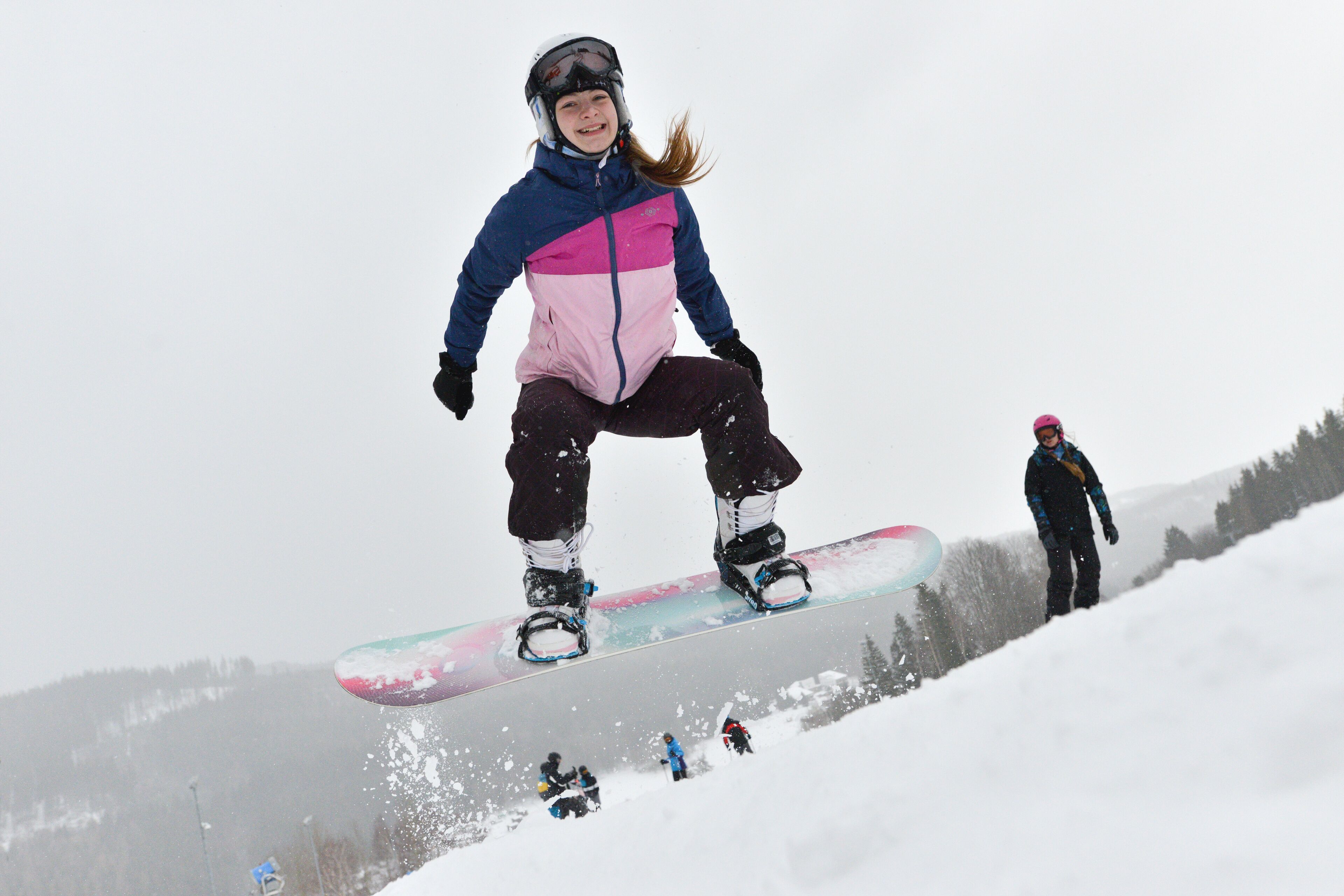 Un snowboardeur en plein saut, en l'air, sur une pente enneigée.