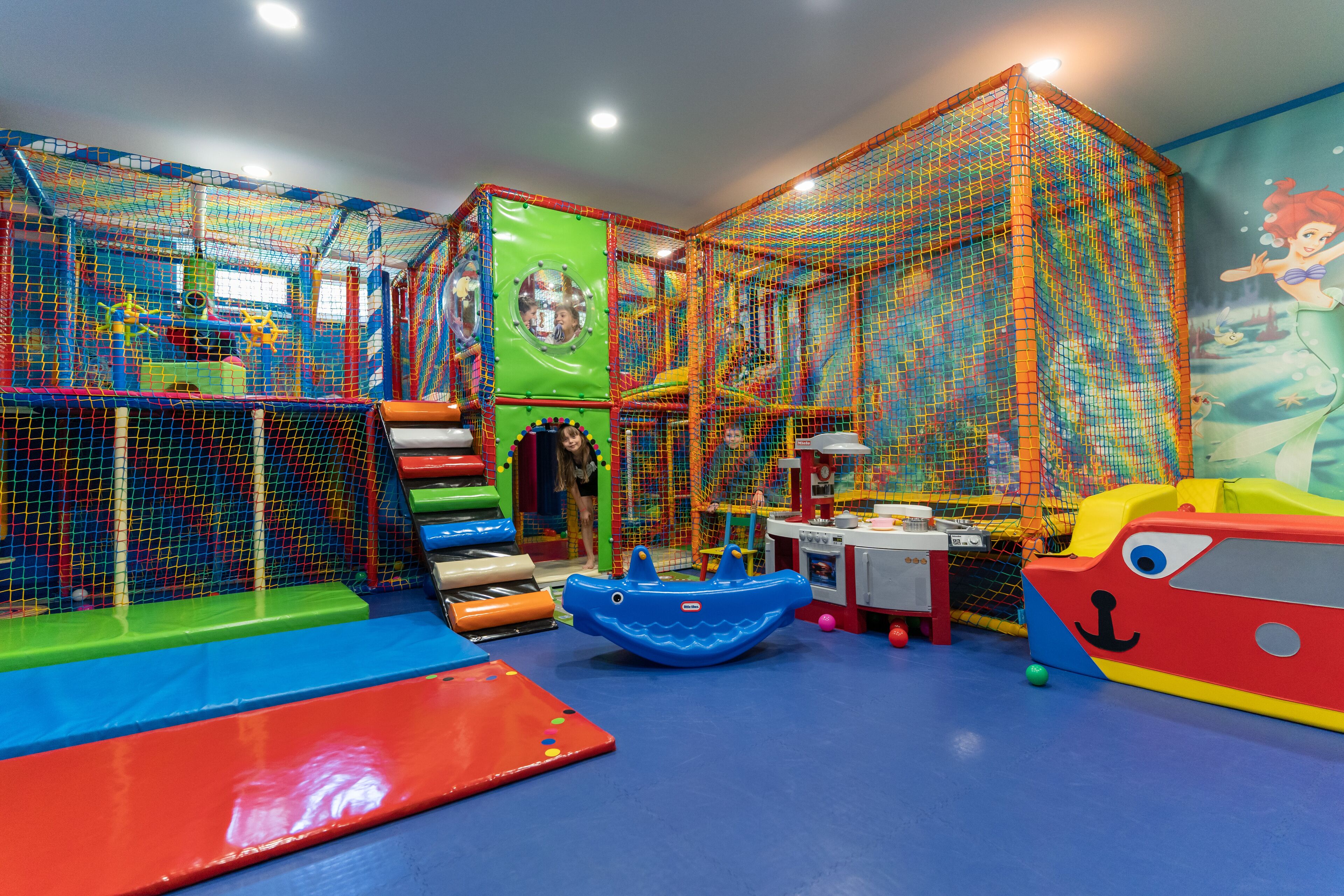 Un área de juegos con una red de escalada, toboganes y una cocina de juguete.
