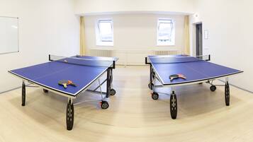 Dos mesas de ping pong en una habitación con suelo de madera clara y paredes blancas.