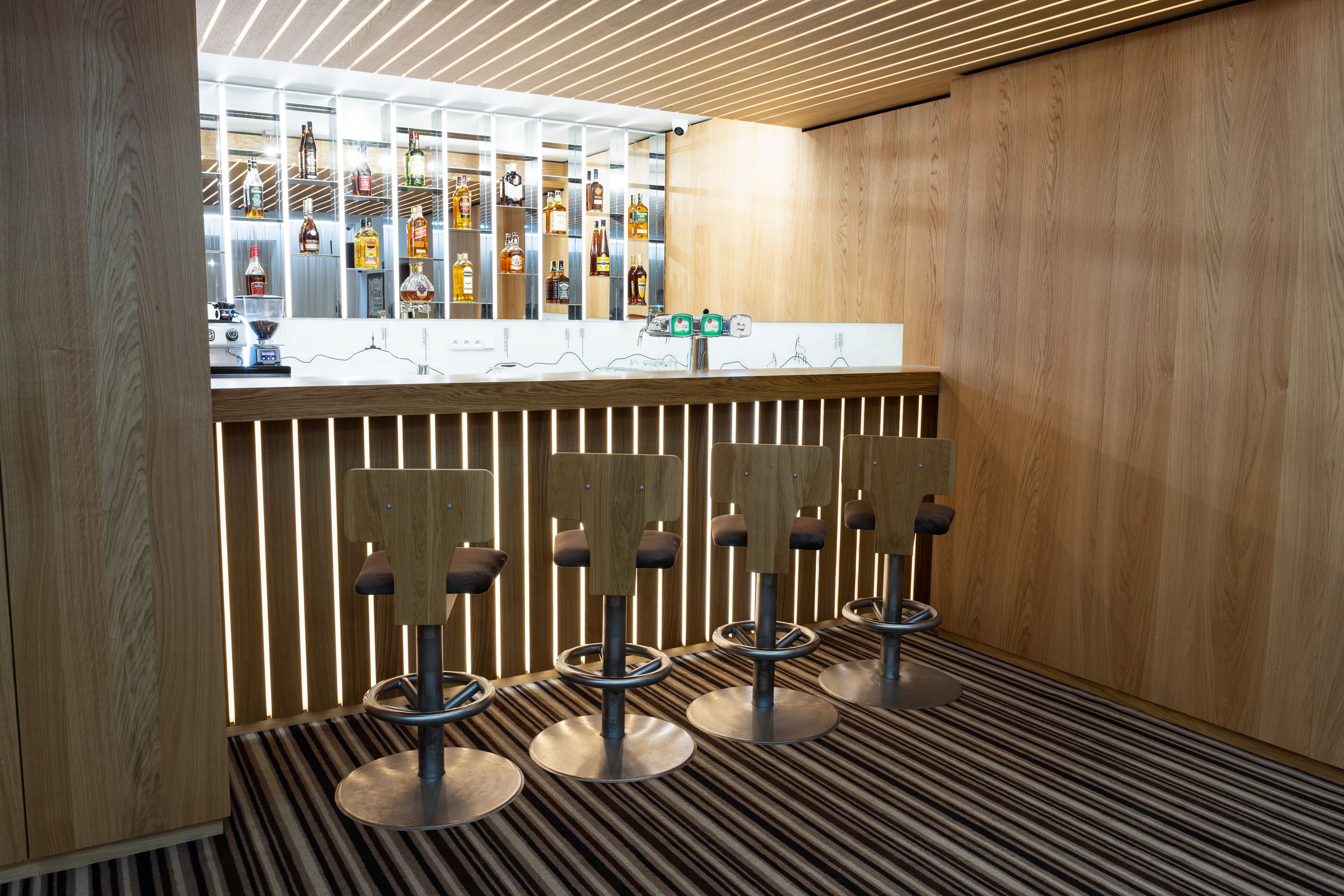 A bar area with multiple stools, a counter with a display of bottles, and a patterned floor.