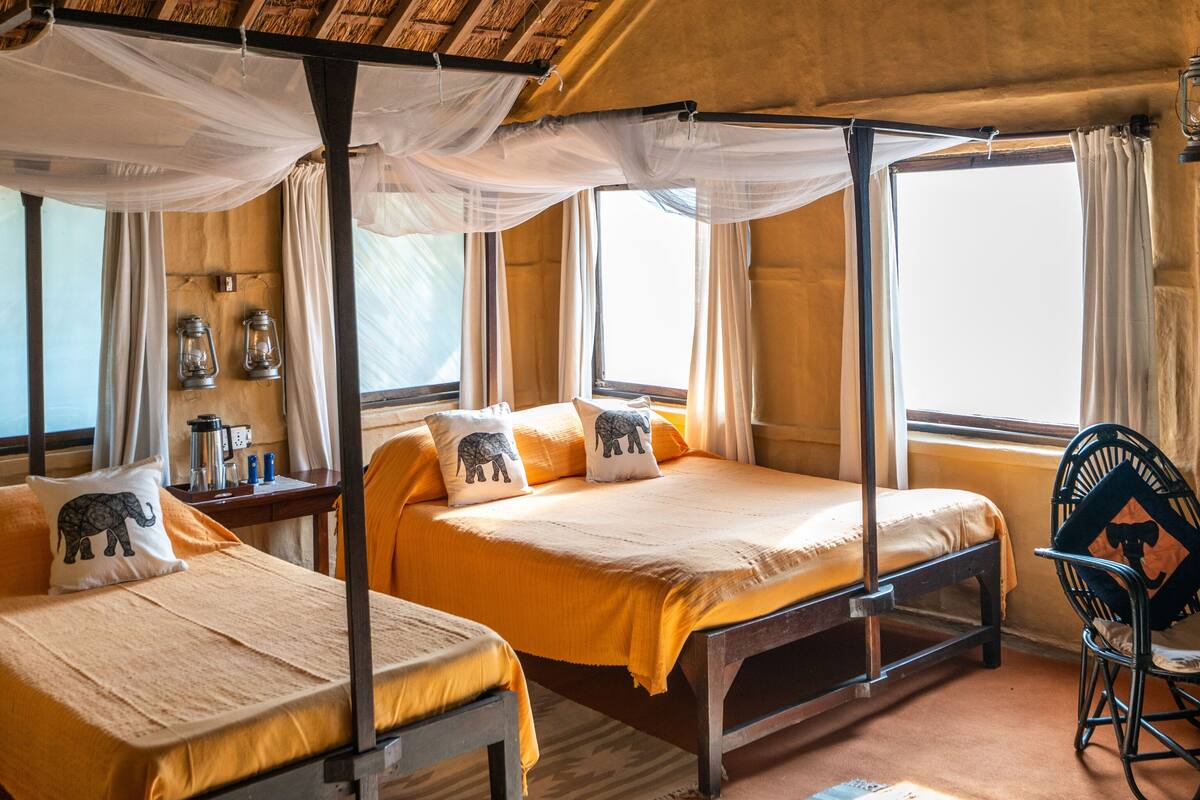 Una habitación con dos camas, mosquitero, una silla y una ventana.