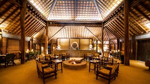 A spacious hall with a high wooden ceiling, a central fire pit, and multiple seating areas. - Tiger Tops Karnali Lodge (Thakudwara)