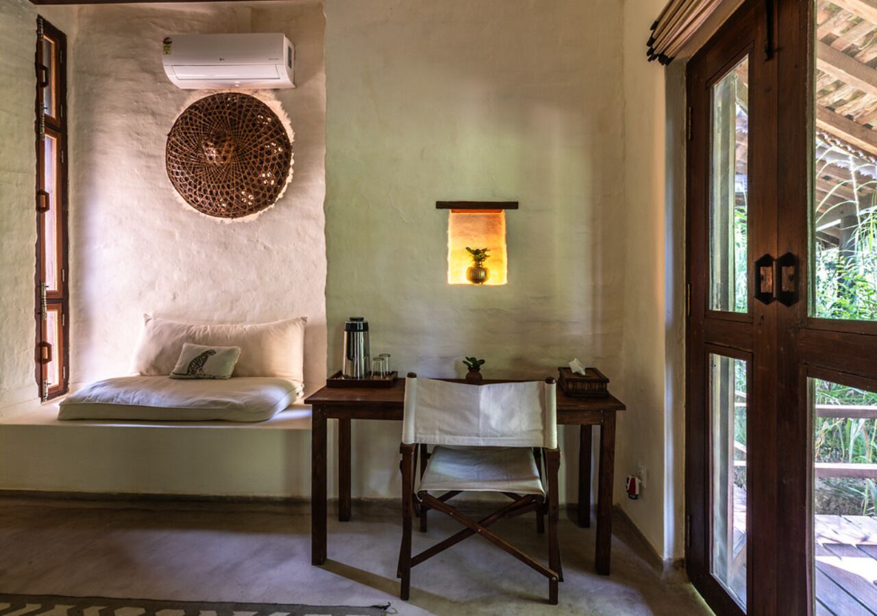 A cozy room with a built-in bench, a wooden chair, a small table, and a wall-mounted shelf with a plant.