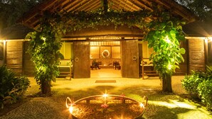 A traditional building with a thatched roof, a stone pathway leading to the entrance, and a small water feature in the foreground. - Tiger Tops Karnali Lodge (Thakudwara)