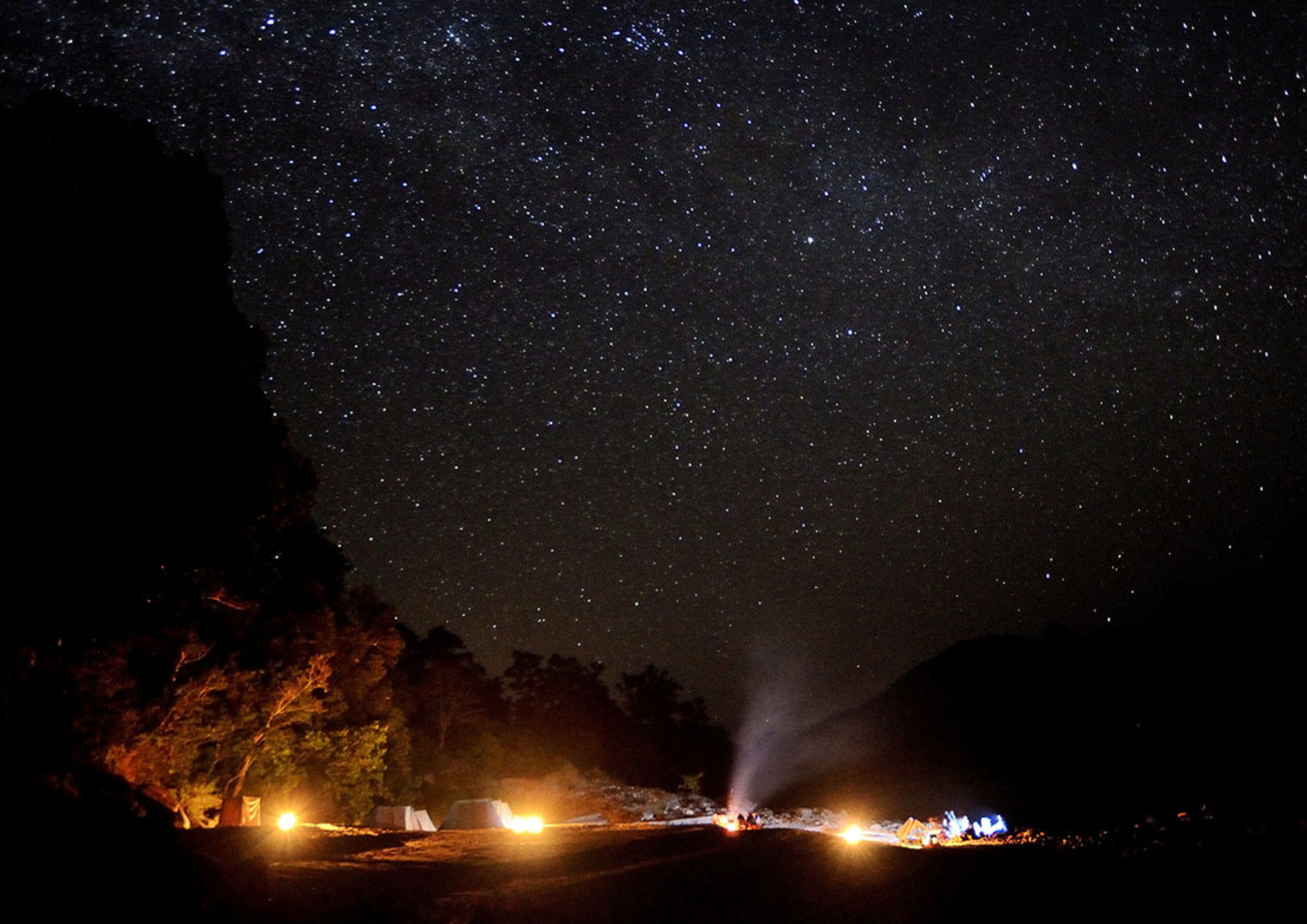 Een sterrenhemel boven een camping met tenten en een rotsachtig landschap.