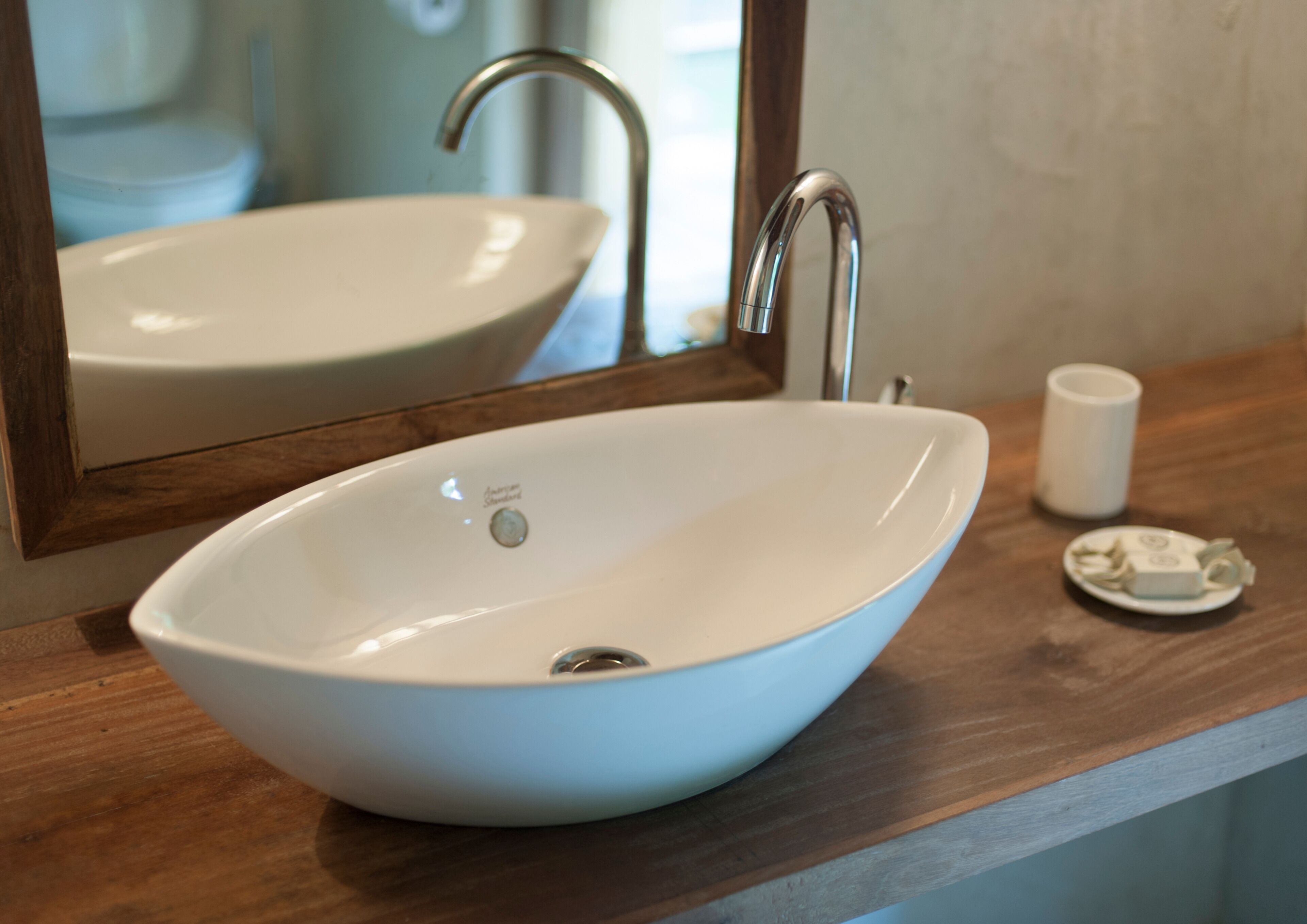 A white oval sink with a single faucet, a small dish, and a cup on a wooden countertop.