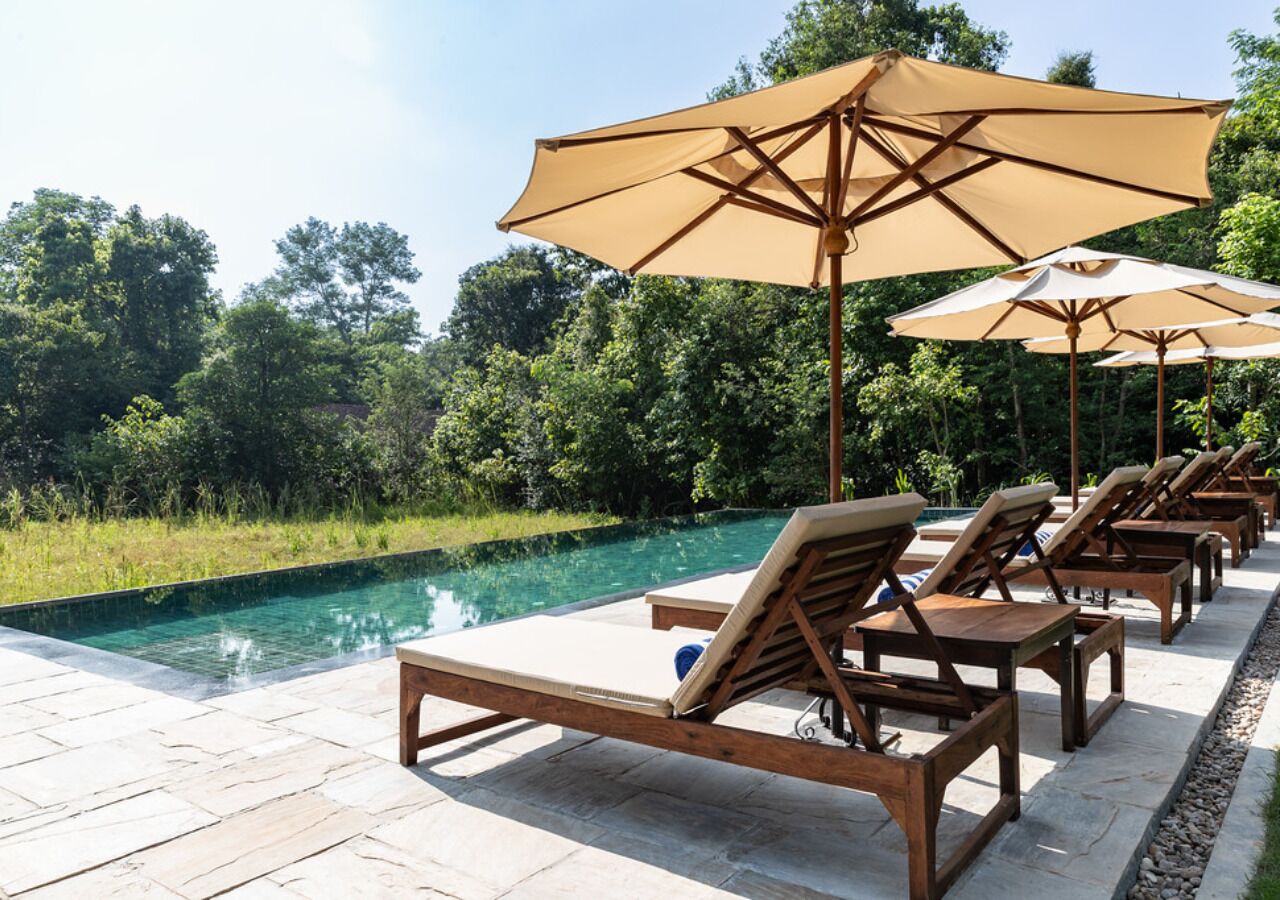 Ein Poolbereich mit Liegestühlen und Sonnenschirmen, umgeben von viel Grün und einem klaren Pool.