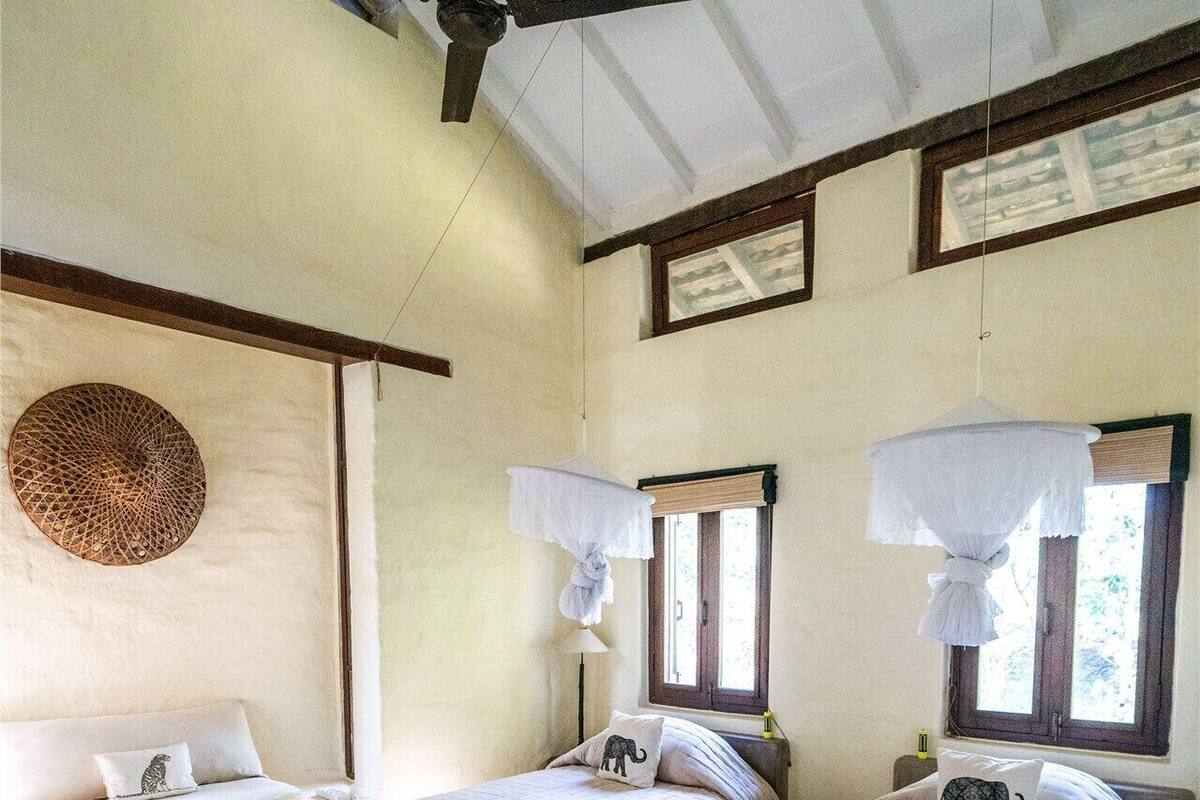 Una habitación con dos camas, un ventilador de techo, un tapiz de pared tejido y una alfombra estampada.
