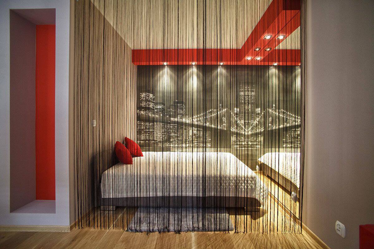 Een slaapkamer met uitzicht op de stad, een bed met een rood kussen en een rode accentmuur.