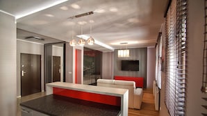 Een moderne keuken met een centraal eiland, een eethoek met een rode accentmuur, en een woonkamer met een bank en een flatscreen-tv.