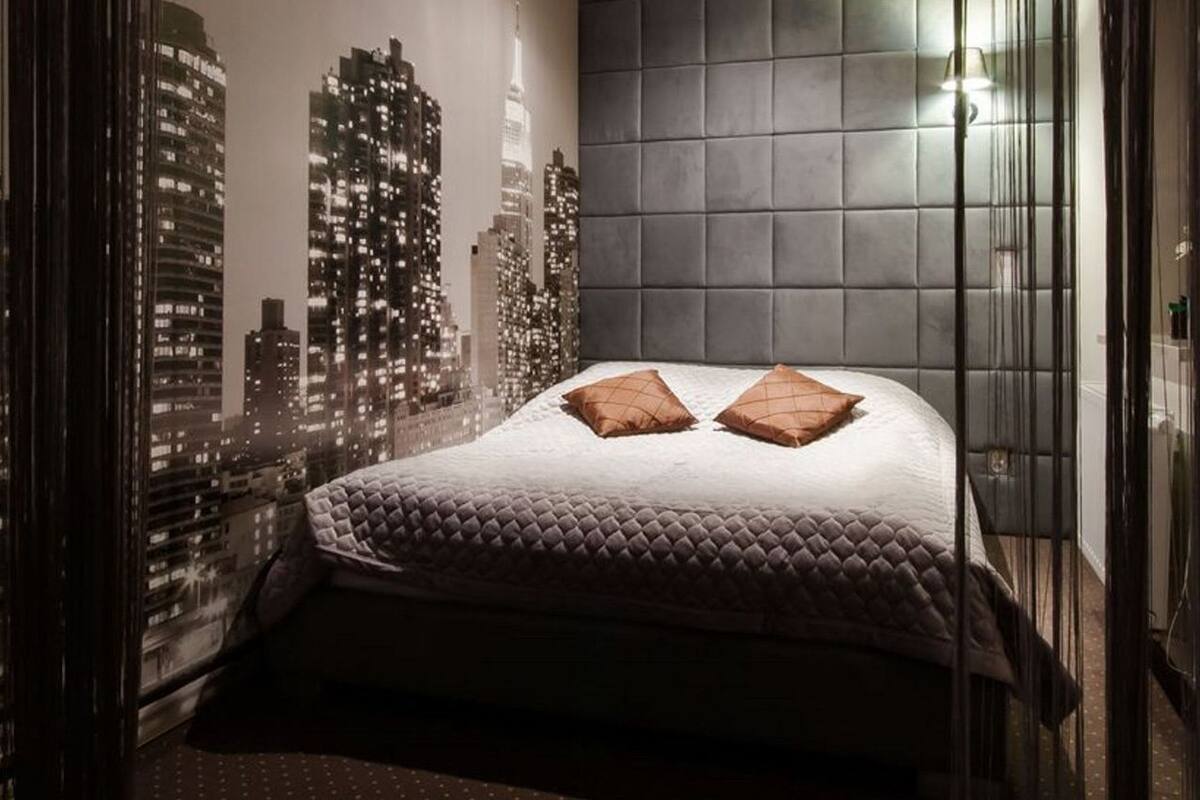 Een slaapkamer met een stadsgezicht muurschildering, een gestoffeerd hoofdeinde en twee kussens.