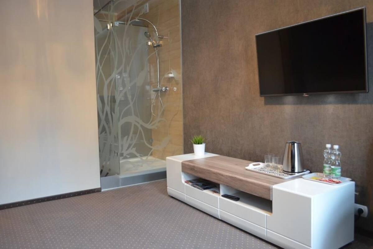 Een moderne badkamer met een douche, een bevestigde televisie, een houten wastafelmeubel en een kleine plant.
