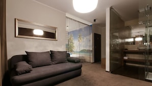 Een moderne woonkamer met een donkere bank, een grote spiegel en een douchecabine van glas.