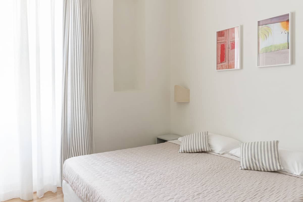 A neatly made bed with striped pillows, a bedside table, and two framed artworks on the wall.