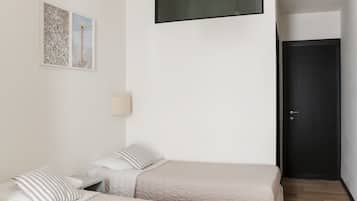 Un dormitorio con dos camas, una mesita de noche, una lámpara de pared y una puerta.