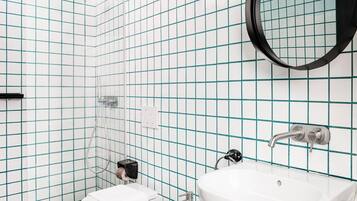 A bathroom with white tiles, a white sink, a toilet, a towel rack, and a shower.