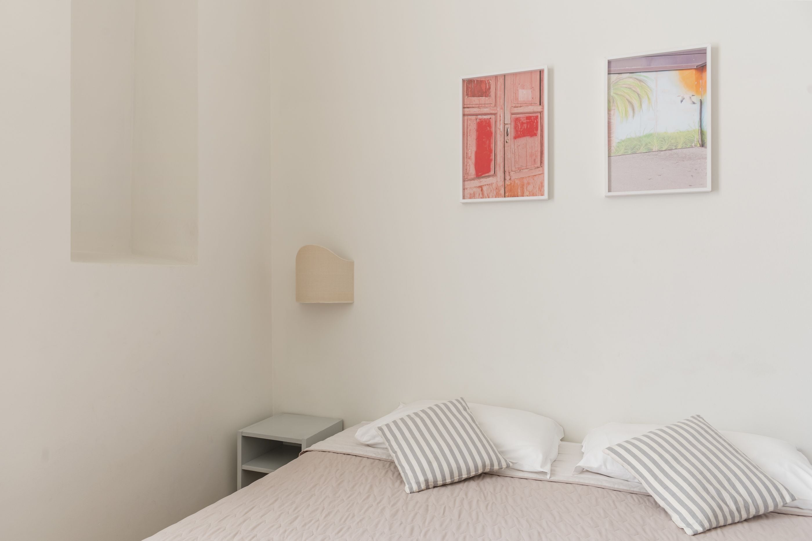 Ein Schlafzimmer mit einem Bett, Kissen, einem Nachttisch und zwei an der Wand befestigten Kunstwerken.