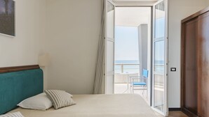 A bedroom with a bed, pillows, a nightstand, and a view of the balcony and ocean. - Hotel Riviera (Anzio)