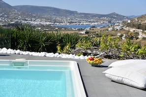 Una piscina con vistas a un pueblo costero, rodeada de plantas y piedras blancas.