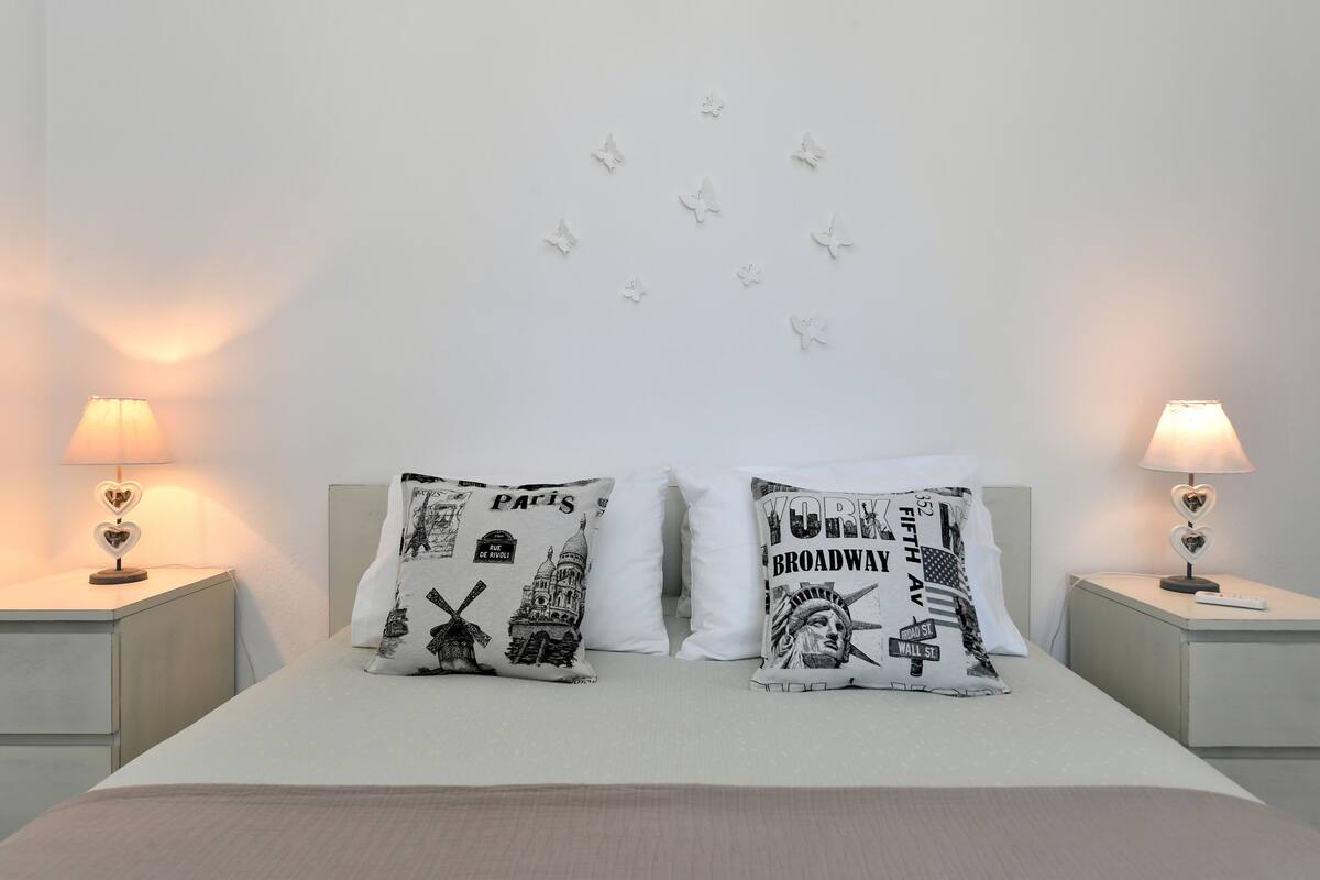Una cama bien hecha con dos almohadones decorativos, cada uno con un diseño de paisaje urbano diferente.