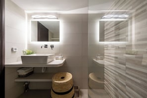 A modern bathroom with a large sink, a mirror, and a toilet. There is a towel rack and a small basket on the floor.