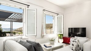 A modern living room with a sofa, a coffee table with a plant, a red storage unit, and a TV. - Azzurro Bianco Suites (Paros)