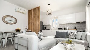 A modern living room with a sofa, coffee table, and a dining area with chairs and a table. - Azzurro Bianco Suites (Paros)