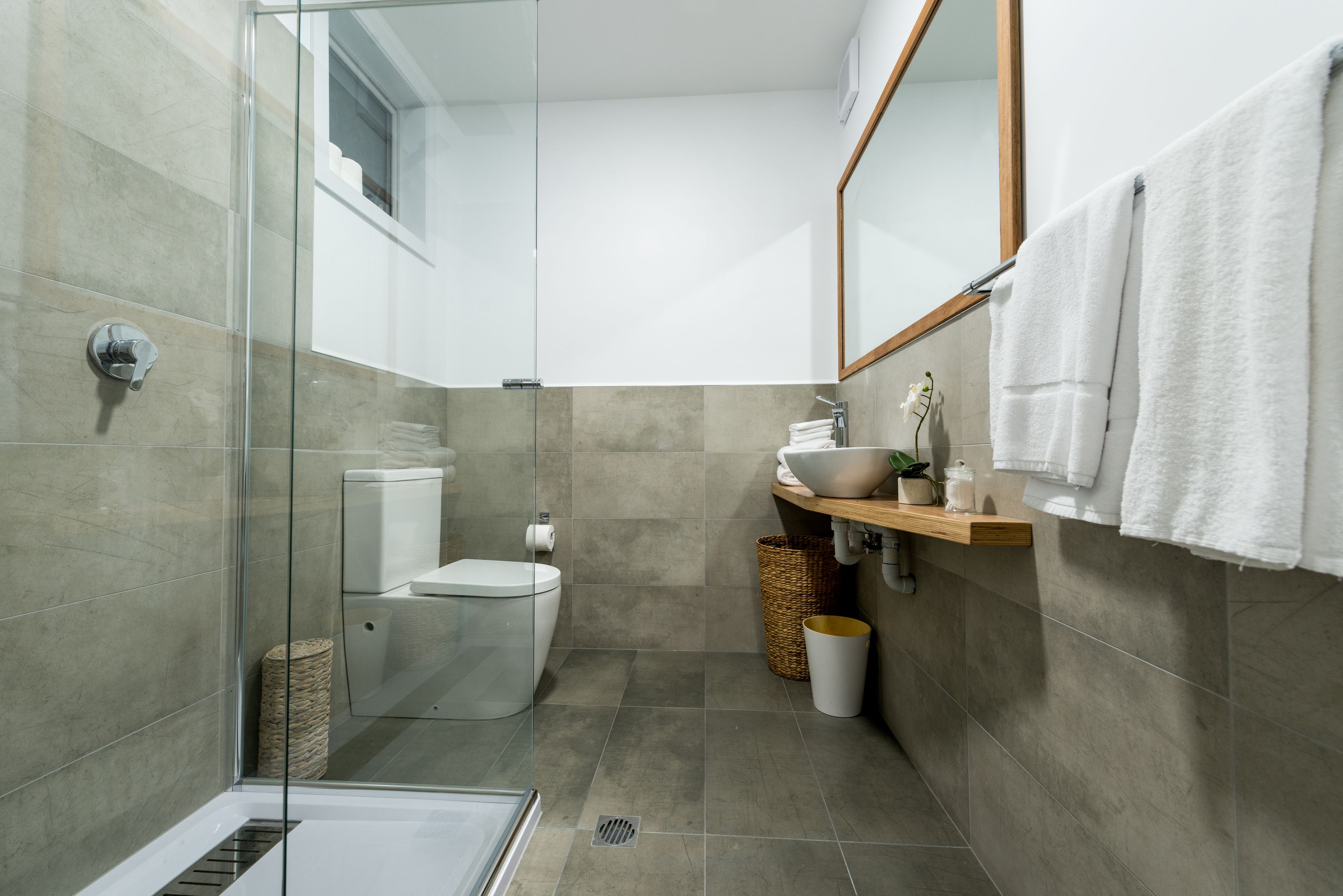A modern bathroom with a glass shower enclosure, a toilet, a sink with a mirror, and a towel rack.