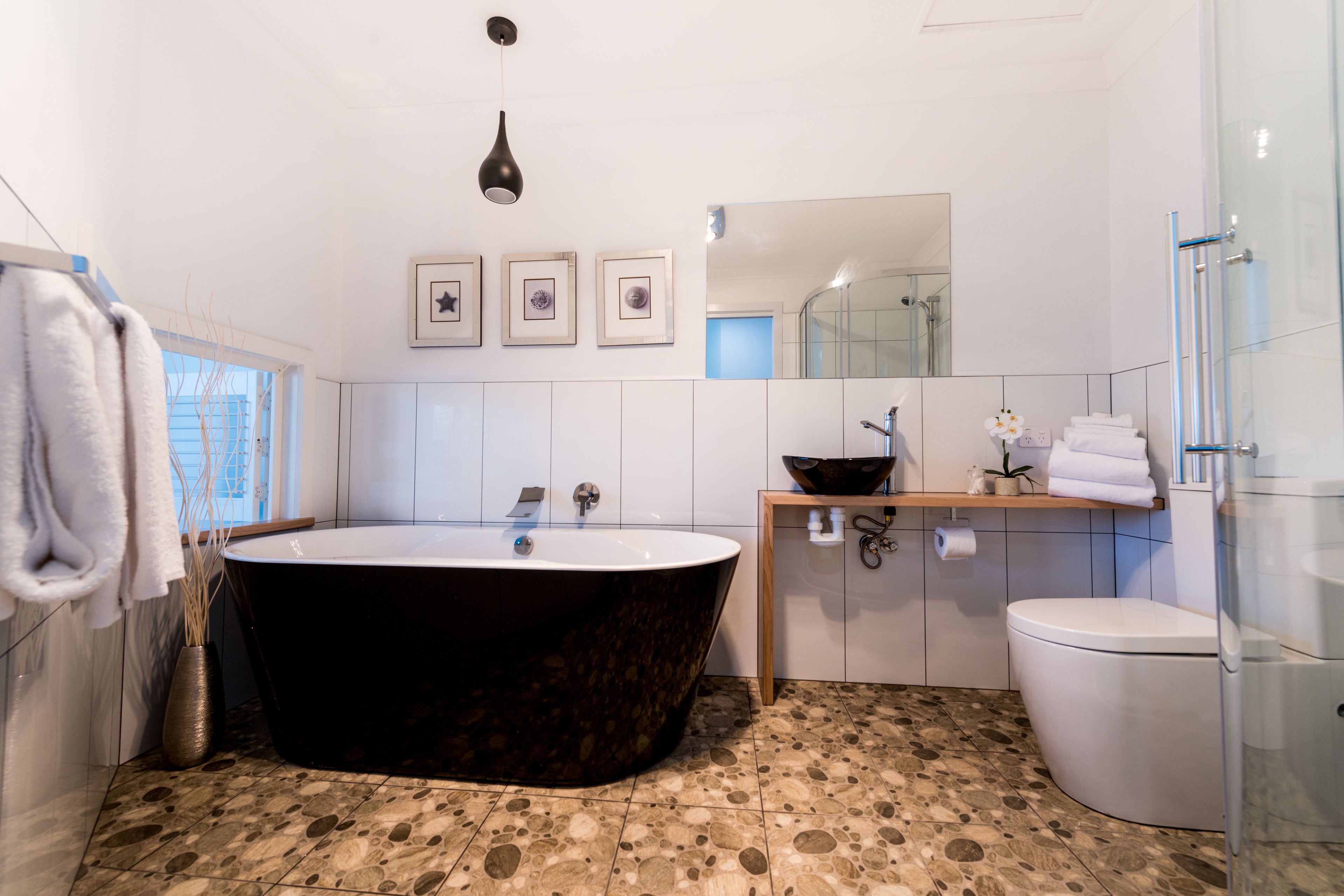 A modern bathroom with a freestanding bathtub, a toilet, a sink with a mirror above, and a shower area.