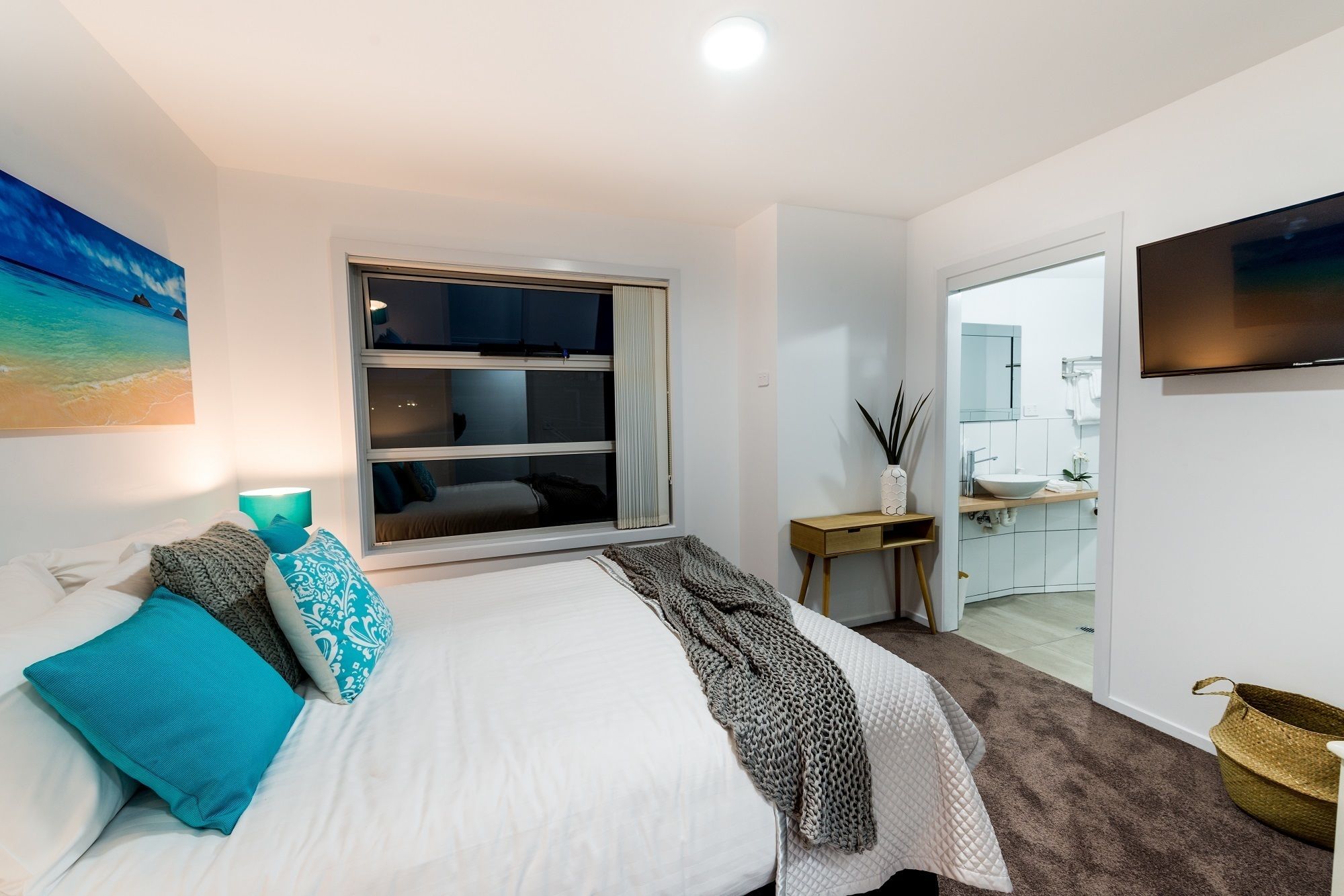 Une chambre à coucher avec un lit, une fenêtre, un téléviseur et une salle de bain visible à travers une porte ouverte.