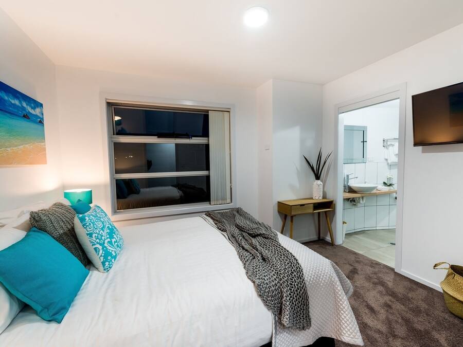 A bedroom with a bed, a window, a TV, and a bathroom visible through an open door.