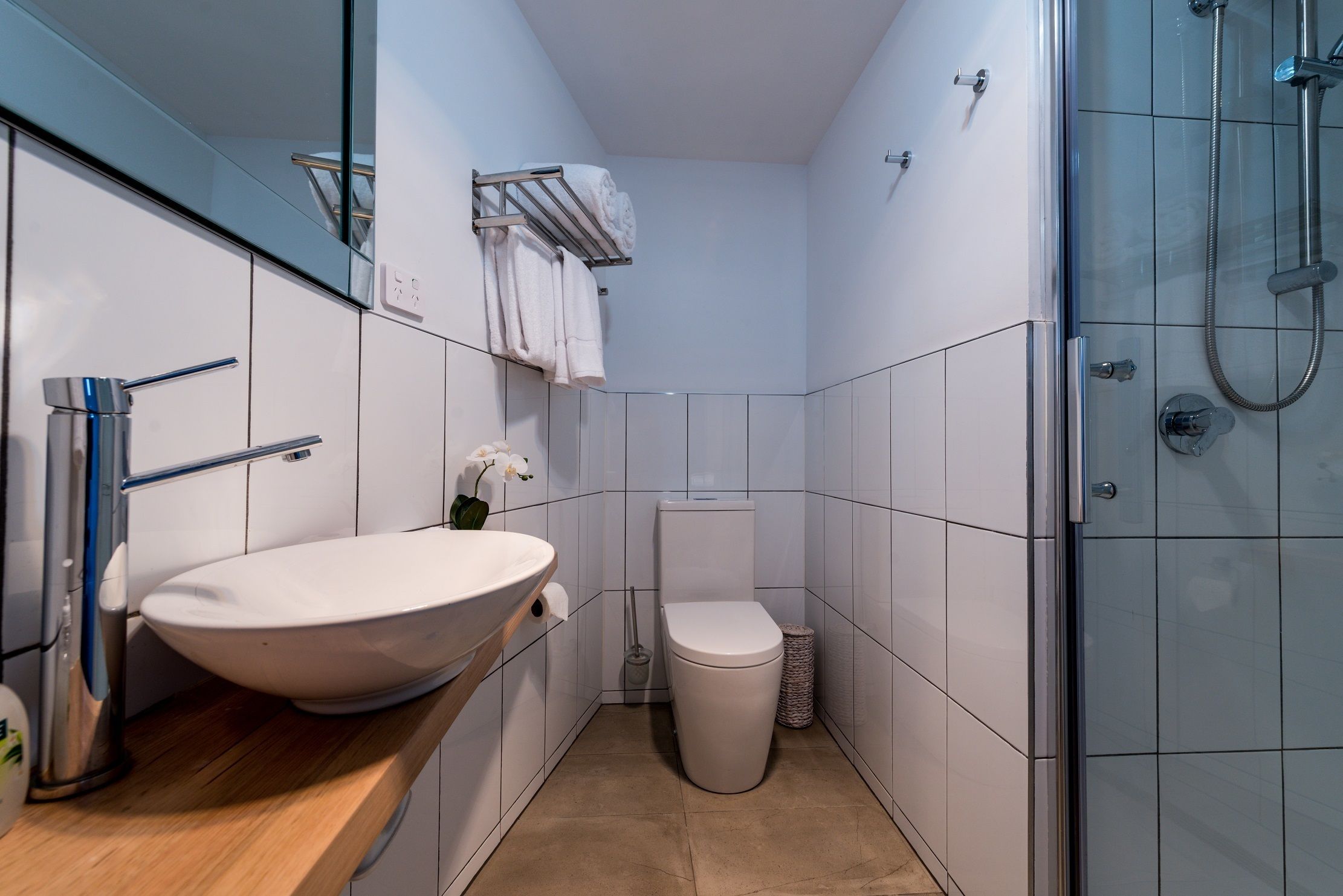 Un baño moderno con un lavamanos grande de color blanco, un inodoro y una zona de ducha con mampara de vidrio.