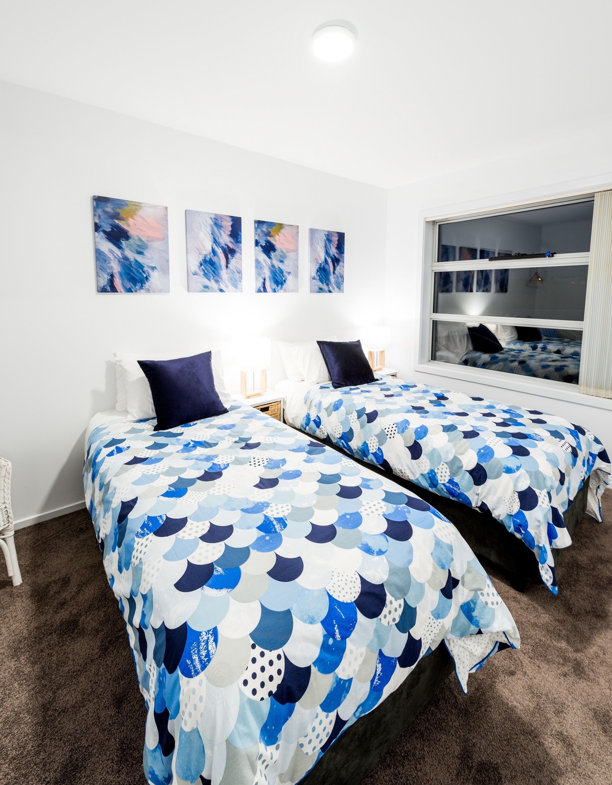 A room with two beds, each with a blue and white patterned bedspread, white pillows, and a window with a view.