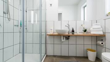 A modern bathroom with a glass shower enclosure, a wooden vanity, a white sink, and a toilet.