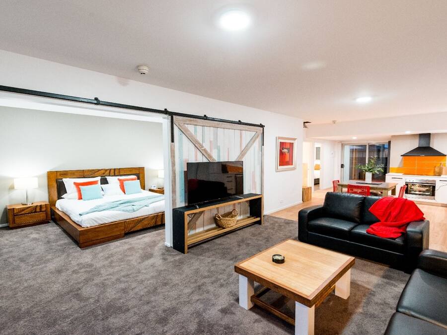 Una sala de estar moderna con una cama, televisor, sofá y una zona de cocina.