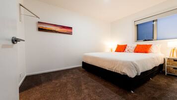 A bedroom with a bed, a nightstand, a lamp, a window, and a painting on the wall.