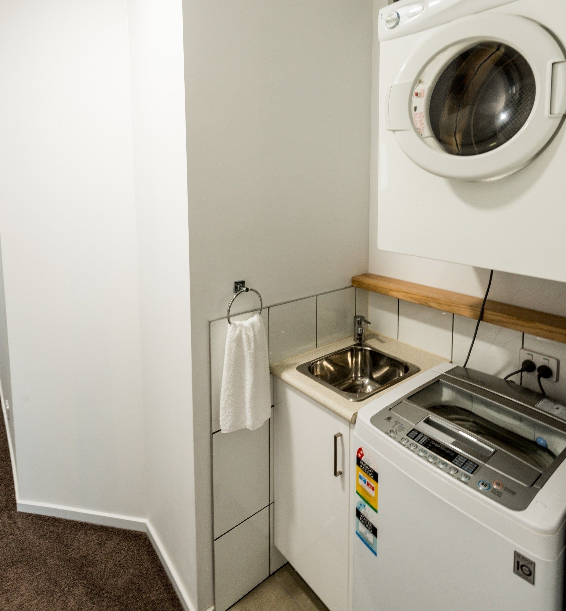 Un espace buanderie compact comprenant un lave-linge, un évier et un étendoir.
