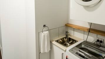 Un espace buanderie compact comprenant un lave-linge, un évier et un étendoir.
