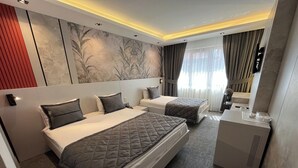 Une chambre d’hôtel avec deux lits, un bureau, un miroir et une grande fenêtre avec des rideaux.