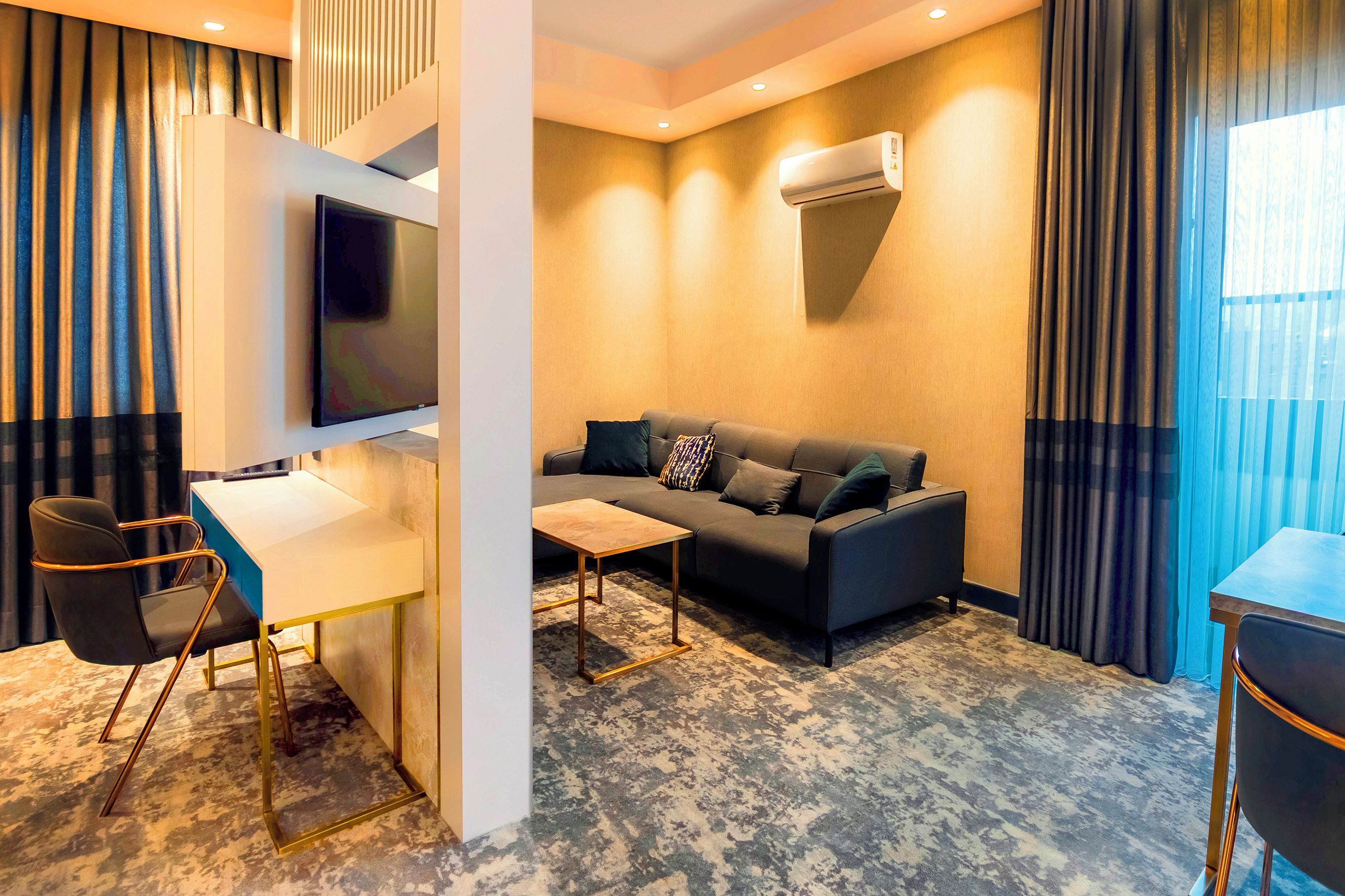 Una habitación de hotel moderna con sofá, escritorio, silla y televisor de pantalla plana.