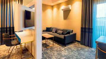 Una habitación de hotel moderna con sofá, escritorio, silla y televisor de pantalla plana.