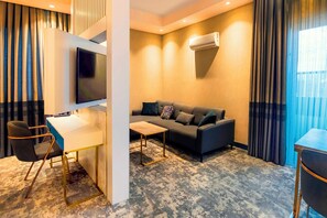 A modern hotel room with a sofa, a desk, a chair, and a flat-screen TV. - Starton Hotel & SPA (Ankara)