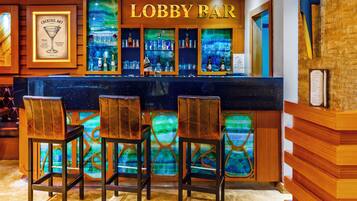 Un bar en el vestíbulo con una barra de madera, taburetes y una obra de arte con temática de cócteles enmarcada.