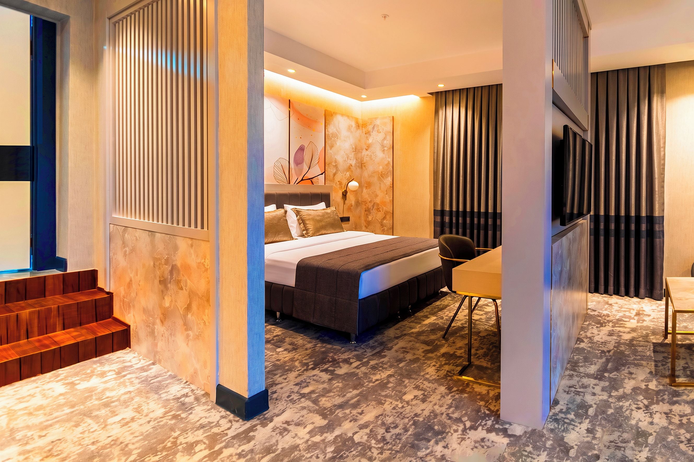 A modern hotel room with a bed, a desk, and a chair. There is a staircase leading to an upper level.